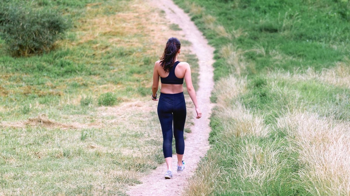 Femme en tenue de sport pratiquant la marche rapide en extérieur dans un parc ensoleillé pour perdre du poids