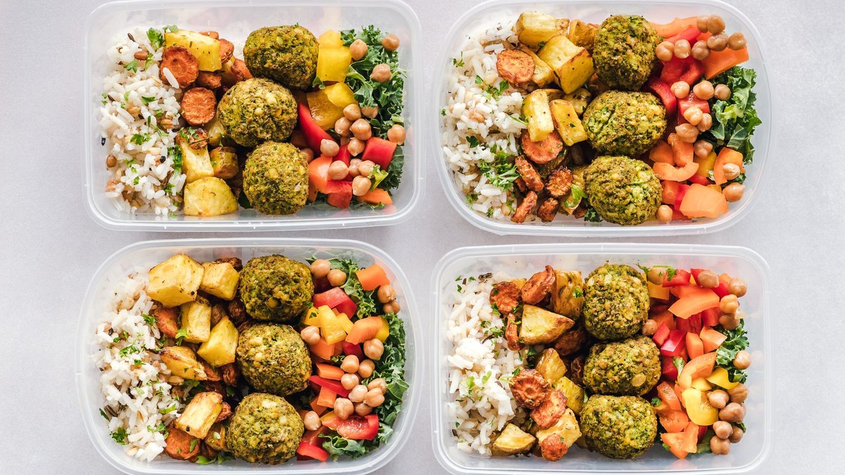 Cinq boîtes en verre remplies de riz, poulet et légumes rôtis alignées sur un plan de travail